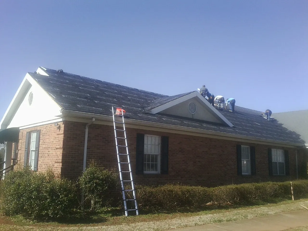 Crew tearing shingles off a brick ranch roof with a ladder set — Metal Roof Repair work by our crew in Garden City